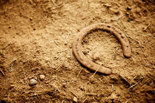 Rusty old horse shoe with a nail still in it lying alone on the dirt floor of an old barn