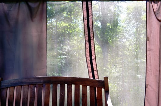 Summerhouse bench and view through net. Shelter for rest in nature.