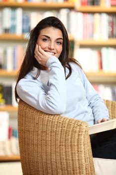 smiling female student with book in hands looking at camera. On a background library