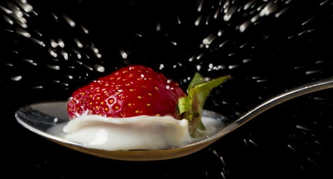 red, ripe strawberry falling in spoon with fresh milk - isolated on lack background