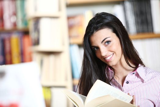 smiling female student with book in hands in a bookstore - model looking at camera. 