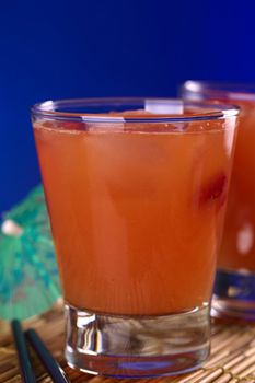 Peruvian cocktail called Pisquina made of pisco, passion fruit and cranberry juice, fresh strawberries, sugar and ice (Selective Focus, Focus on the front rim of the glass)