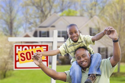 Happy African American Father and Son in Front of New Home and Sold Real Estate Sign.