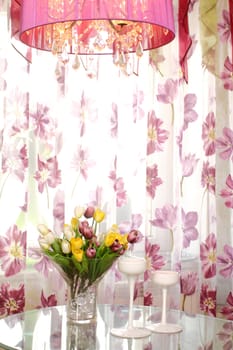 bouquet of multi-colored tulips on a glass table in a glass vase against a window, a vertical shot