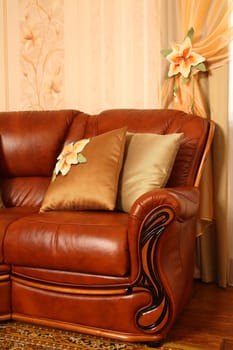 Brown leather sofa with beautiful pillows near a window with a beautiful curtain. Vertical shot, close up. The embroidery isn't a handiwork, this repetition of drawing on wall-paper.