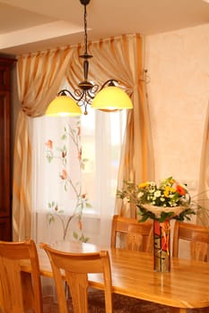 bunch of flowers in a vase on a table against a window with a beautiful curtain