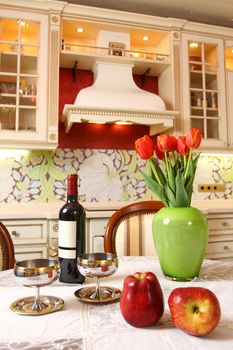the wine bottle, two glasses, apples and bouquet of tulips in a green vase on a kitchen table, a vertical shot, option 2