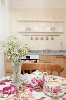 interior of the modern apartment, table with a teapot, a cup and a bunch of flowers, a vertical shot