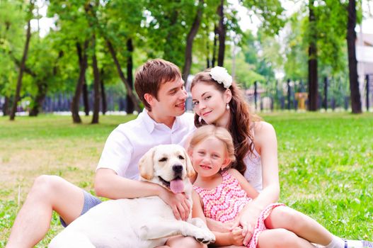 Happy young family with Labrador is resting in the park