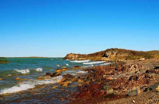Stony coast leaving for horizon with blue sea water