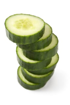 Photo of a cucumber cut into thick slices and stacked over a white background.
