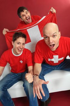 Photo of three male Swiss sports fans cheering for their team.
