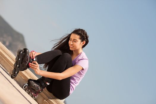 Girl going rollerblading sitting putting on inline skates outdoors