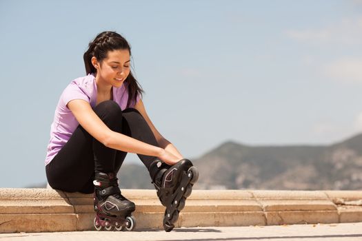 Girl going rollerblading sitting putting on inline skates outdoors