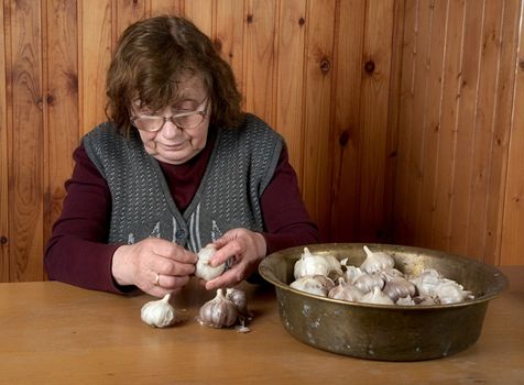 The old woman touches garlic sitting for a table
