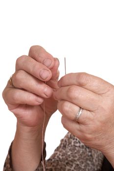 Hands of the old woman pass  thread in  needle on white background