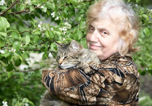 The old woman holds on hands cat against a blossoming tree