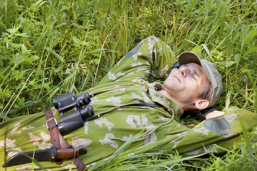 A man dressed in camouflage suit rests on the grass