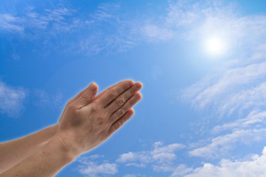 Praying hands against blue sky with clouds