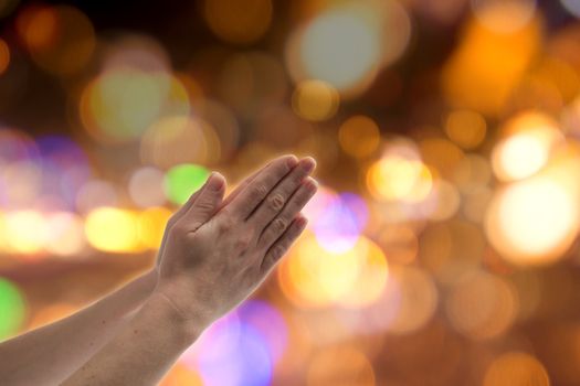 Praying hands against a colorful lights background