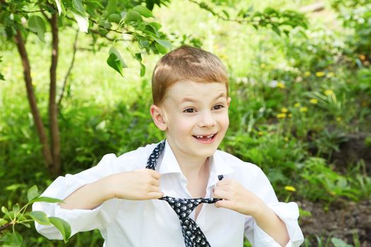 The little boy unties a tie against green leaves