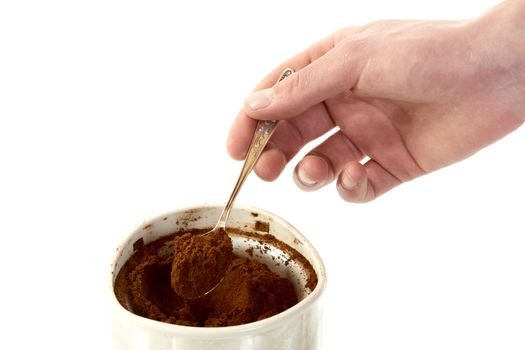 The man's hand with spoon takes coffee from  coffee grinder on a white background
