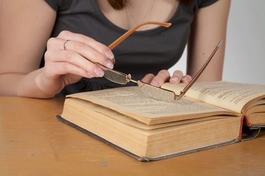 The girl holds glasses and reads the old book