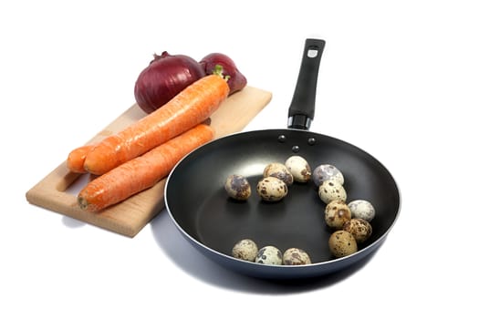 Carrots, onions on a chopping board and quail eggs on  frying pan