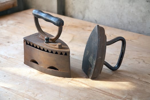 Two old irons on a table in beams of the coming sun