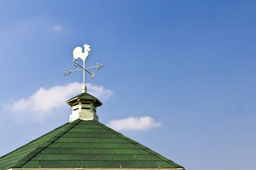 Rooster weather vane on roof and blue sky background