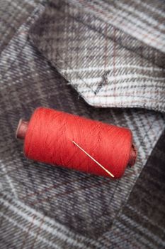 Red sewing spool with needle on a flannel fiber. Close-up photo