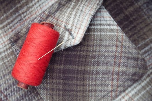 Red sewing spool with needle on a flannel fiber. Close-up photo