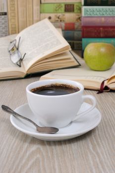 A cup of coffee on the table against the background of an open book with a notebook