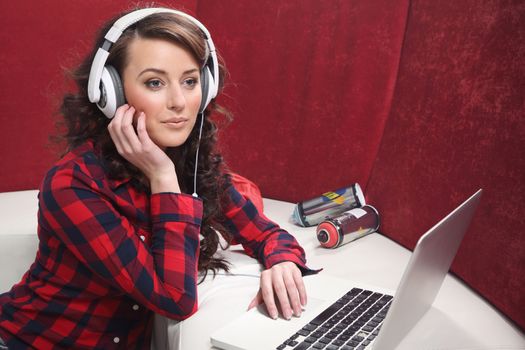 Young girl with laptop listen to music with headphones, near the sofa.