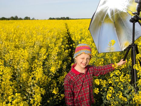 little photographer assistant hold umbrella stand  a yellow canola field