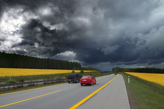 Highway between the blooming fields of rapeseed. The storm clouds.