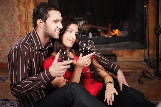 Happy couple in love enjoying wine near fireplace