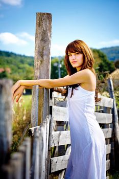 Pretty country girl in white dress on a sunny day standing near railing