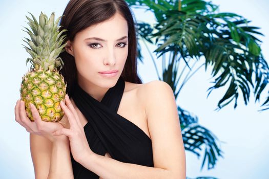 Pretty woman holding pineapple in front of a palm tree