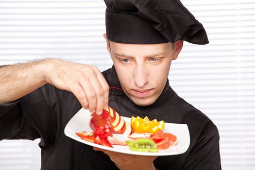 chef in black uniform decorating delicious fruit plate