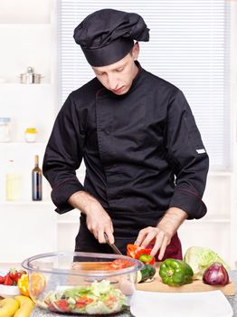 chef in black uniform cutting bell peppers on board