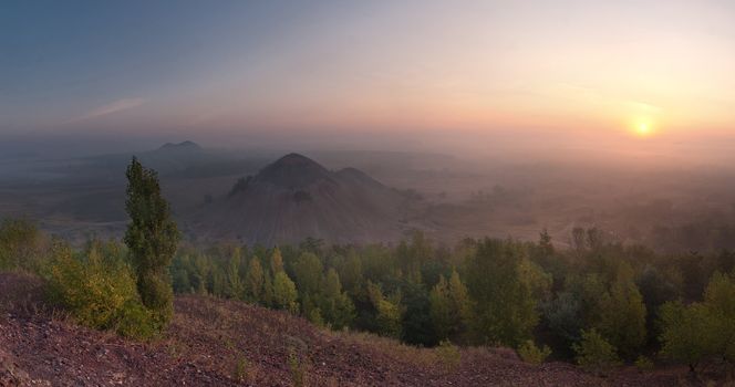 The top view landscape on valley with waste heaps in fog and rising sun