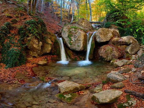 A waterfall in the mountains, around autumn forest with yellow foliage and the blue sky, outdoors