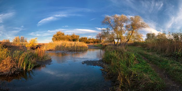 Colorful autumn landscape on evening river with beautiful clouds in the sky. Panorama