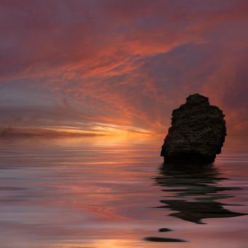 Landscape with the lonely rock at the ocean and the colourful sunset which was reflected in water