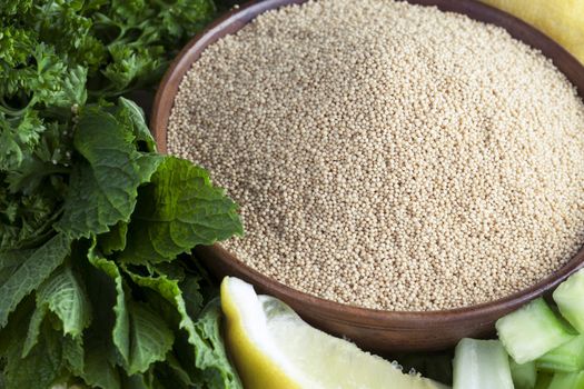 Bowl of amaranth seeds surrounded by mint, parsley and a lemon wedge.
