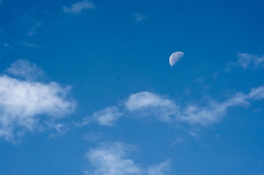 Bright blue morning sky with the half moon and clouds