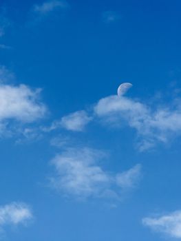 Bright blue morning sky with the half moon and clouds