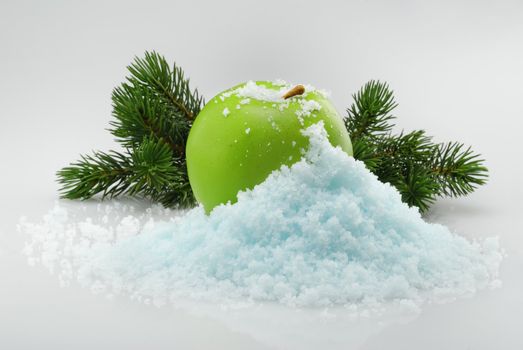 Green delicious Christmas apple in snow with christmas tree branches on the background