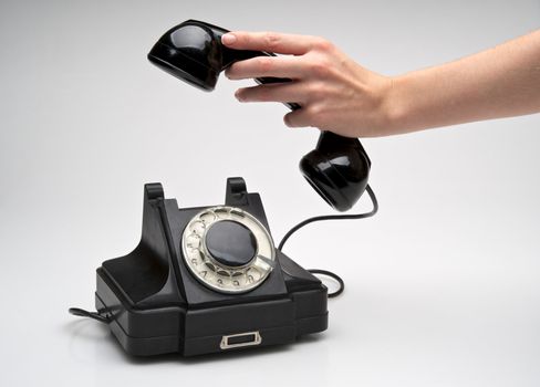 woman hand hanging up the handset of an old black telephone isolated ocer white background